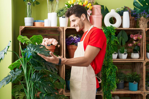 Jeune homme hispanique fleuriste souriant confiant toucher plante feuille à la boutique de fleurs - Photo, image