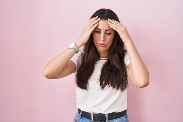 Young brunette woman standing over pink background with hand on head, headache because stress. suffering migraine.  - Zdjęcie, obraz