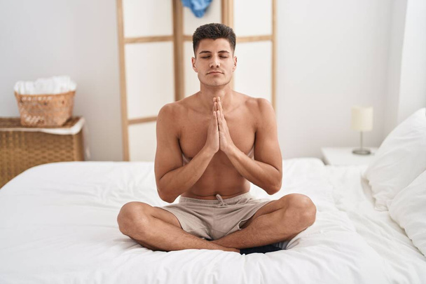 Young hispanic man doing yoga exercise sitting on bed at bedroom - Photo, image