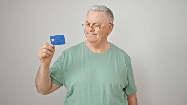 Седовласый мужчина средних лет улыбается уверенно держа кредитку на изолированном белом фоне - Фото, изображение