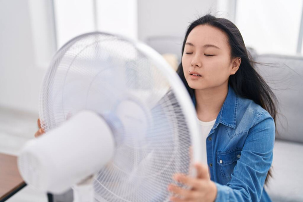 Mladá Číňanka pomocí ventilátoru sedí na pohovce doma - Fotografie, Obrázek
