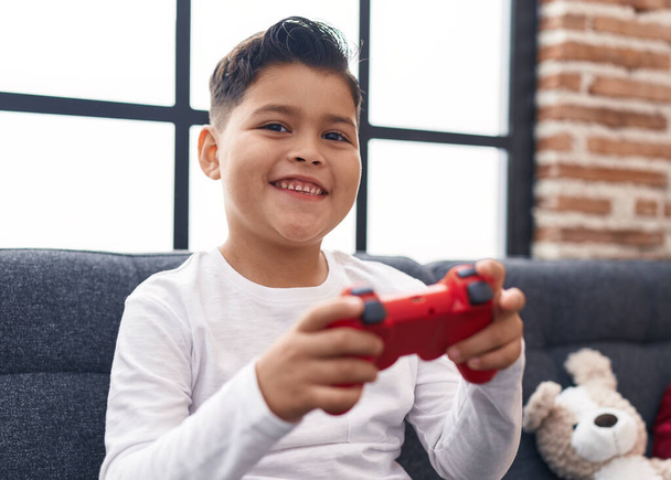 Evdeki kanepede oturmuş video oyunu oynayan sevimli İspanyol çocuk. - Fotoğraf, Görsel