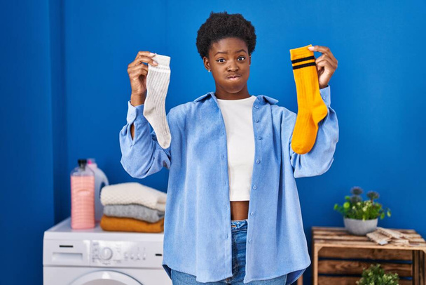 African american woman holding clean andy dirty socks puffing cheeks with funny face. mouth inflated with air, catching air.  - Фото, зображення