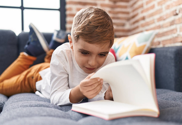 Чарівний іспаномовний хлопчик читає книгу, що лежить на дивані вдома
 - Фото, зображення