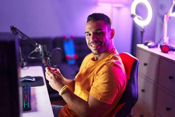 Junger hispanischer Mann streamt mit Computer und Smartphone in Spielhalle - Foto, Bild