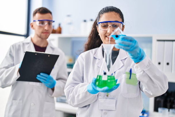 Man and woman wearing scientist uniform write on document measuring liquid at laboratory - Foto, Imagem