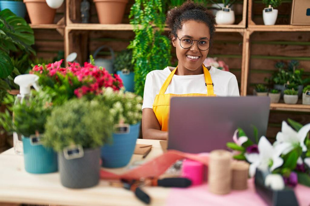 Florista mujer afroamericana sonriendo confiada usando laptop en floristería - Foto, Imagen
