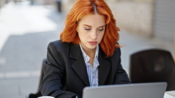 Young redhead woman business worker using laptop with relaxed expression at coffee shop terrace - Photo, Image