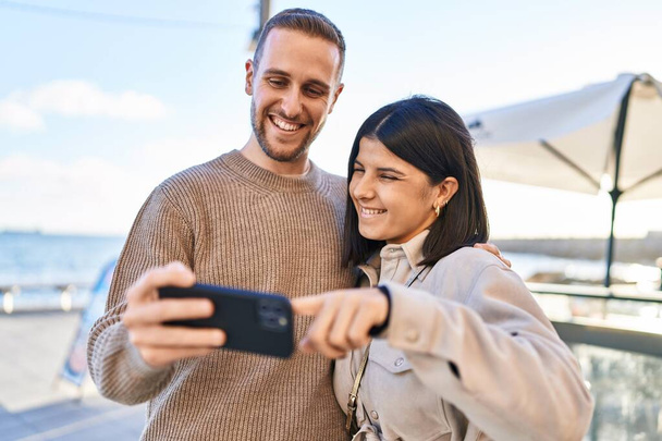 Férfi és nő pár mosolygós magabiztos segítségével smartphone a tengerparton - Fotó, kép