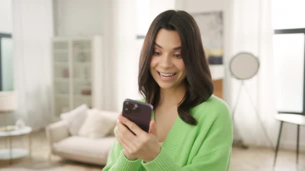 Portrait of happy elegant brunette woman typing in mobile phone indoors. Closeup cheerful girl standing with smartphone in stylish loft apartment background. Smiling lady holding cellphone in hands 4K - Footage, Video