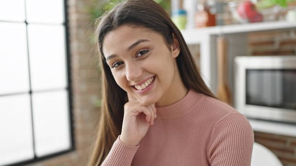 Jovem bela mulher hispânica sorrindo confiante sentado na mesa na sala de jantar - Foto, Imagem