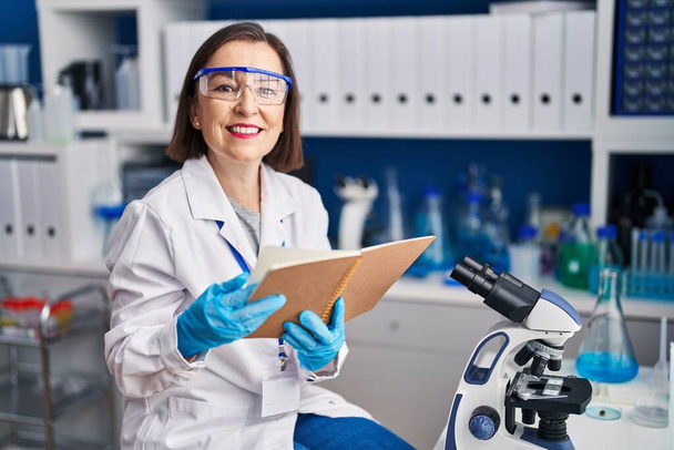 Wissenschaftlerin mittleren Alters lächelt zuversichtlich beim Lesen von Buch im Labor - Foto, Bild
