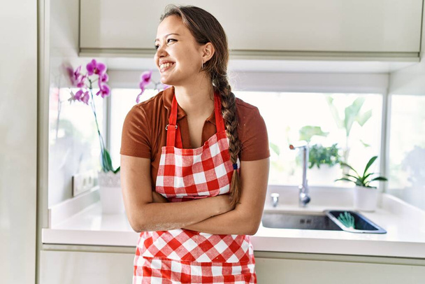 Молодая красивая латиноамериканка в фартуке, стоящая со скрещенными руками на кухне. - Фото, изображение