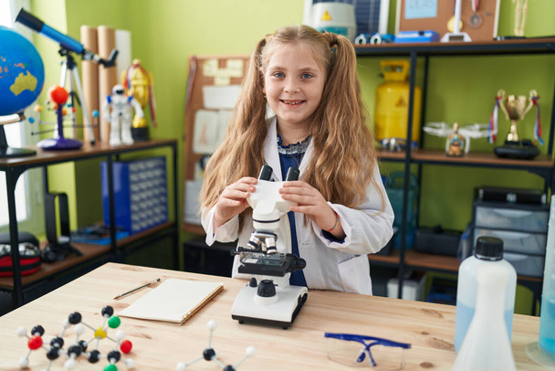 Adorable chica rubia estudiante sonriendo confiado usando microscopio en el aula de laboratorio - Foto, imagen