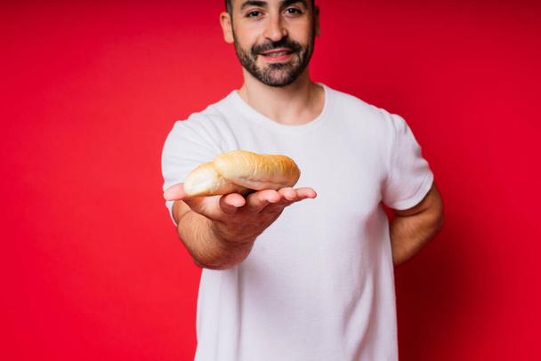 Homme avec du pain fraîchement cuit dans les mains isolé sur fond rouge studio - Photo, image