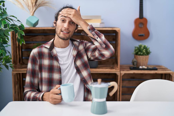 Young hispanic man drinking coffee from french coffee maker stressed and frustrated with hand on head, surprised and angry face  - Fotografie, Obrázek