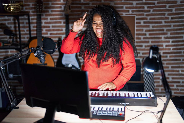 Plus size hispanic woman playing piano at music studio pointing finger up with successful idea. exited and happy. number one.  - Foto, Imagen