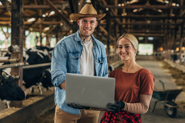 Front view of a Caucasian woman and man holding a laptop in a barn. - 写真・画像