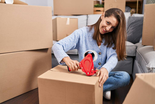 Young woman packing cardboard box at new home - Φωτογραφία, εικόνα