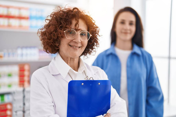Дві жінки фармацевт і клієнт посміхаються впевнено стоячи в аптеці
 - Фото, зображення