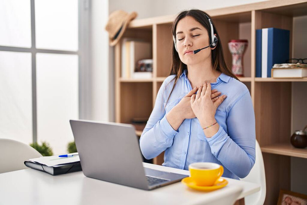 Young brunette woman wearing call center agent headset smiling with hands on chest with closed eyes and grateful gesture on face. health concept.  - Fotografie, Obrázek