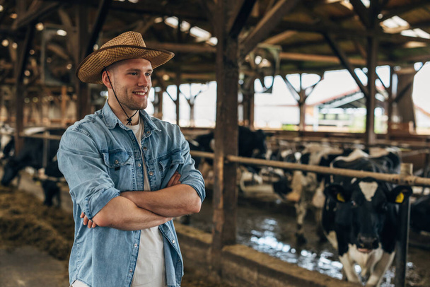 Happy cowboy standing in a stale with cows in it. - Fotoğraf, Görsel