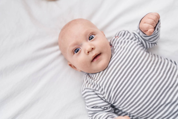 Adorável bebê caucasiano sorrindo confiante deitado na cama no quarto - Foto, Imagem