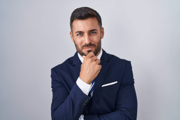 Handsome hispanic man wearing suit and tie looking confident at the camera smiling with crossed arms and hand raised on chin. thinking positive.  - Photo, Image
