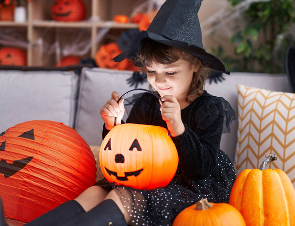 Adorable chica hispana teniendo fiesta de halloween buscando cesta de calabaza en casa - Foto, Imagen