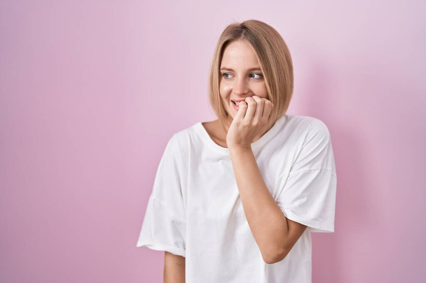 Young caucasian woman standing over pink background looking stressed and nervous with hands on mouth biting nails. anxiety problem.  - Foto, afbeelding