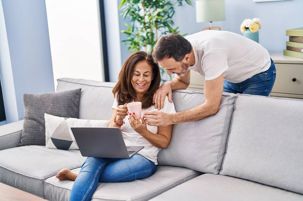 mężczyzna i kobieta w średnim wieku para za pomocą laptopa picia kawy w domu - Zdjęcie, obraz