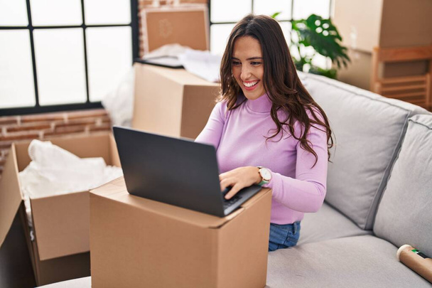 Junge hispanische Frau lächelt selbstbewusst mit Laptop im neuen Haus - Foto, Bild
