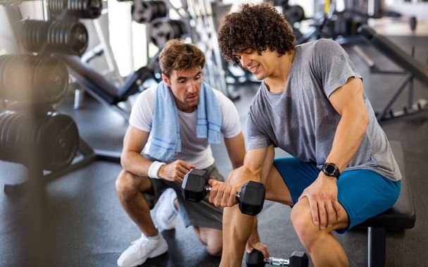 Fitness, sport, exercising and diet concept. Happy fit man exercising together with his personal trainer, friend in gym. - Foto, immagini