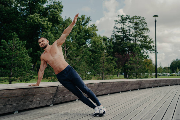 Aktivsportler trainiert im Freien, posiert in Seitenplanken, trainiert starke Muskeln, atmet frische Luft. Bauchmuskeltraining. - Foto, Bild