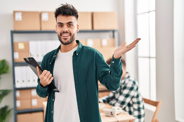 Zwei hispanische Männer, die in einem kleinen E-Commerce-Geschäft arbeiten, feiern ihre Leistung mit glücklichem Lächeln und Siegerausdruck mit erhobener Hand  - Foto, Bild