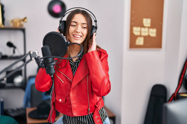 Jonge mooie Spaanse vrouw muzikant glimlachend zelfverzekerd zingen lied in muziekstudio - Foto, afbeelding