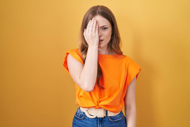 Caucasian woman standing over yellow background yawning tired covering half face, eye and mouth with hand. face hurts in pain.  - Fotografie, Obrázek