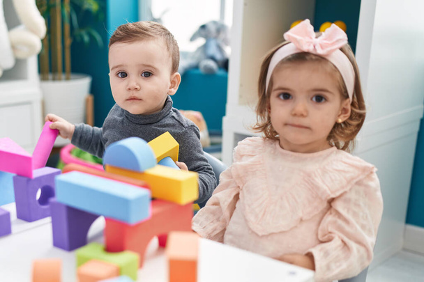 Очаровательный мальчик и девочка играют со строительными блоками, сидя на столе в детском саду - Фото, изображение