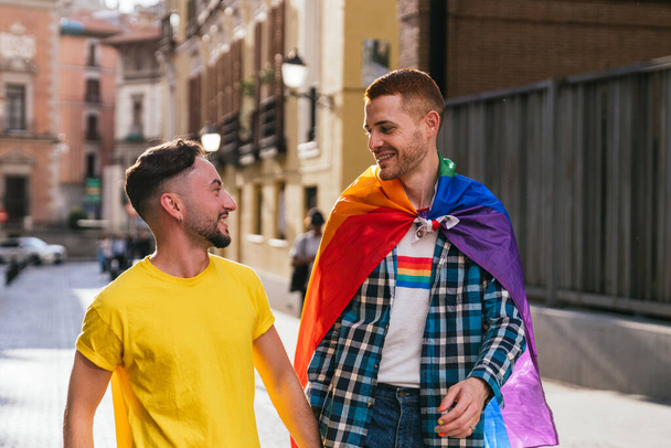 Крупним планом фотографія двох гей-друзів, що йдуть рукою в руці, освітлена заходом сонця. Яскраві аксесуари LGBTQ прикрашають їх
. - Фото, зображення