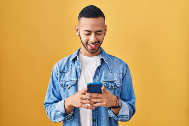 Young hispanic man using smartphone typing message winking looking at the camera with sexy expression, cheerful and happy face.  - Foto, immagini