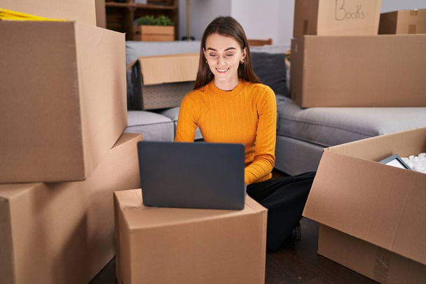Young caucasian woman using laptop sitting on floor at new home - Foto, imagen