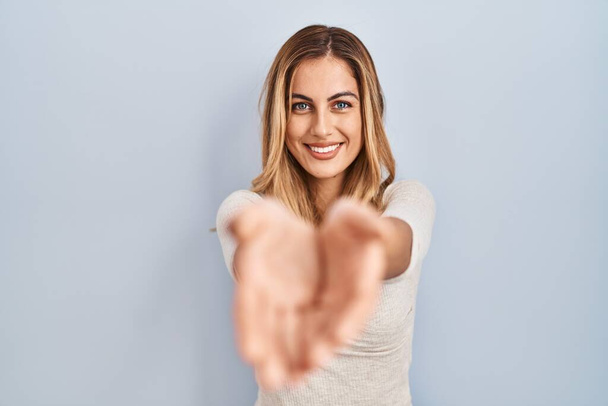 Young blonde woman standing over isolated background smiling with hands palms together receiving or giving gesture. hold and protection  - Foto, imagen