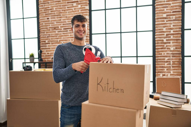Jeune homme hispanique souriant confiant emballage boîte en carton à la nouvelle maison - Photo, image