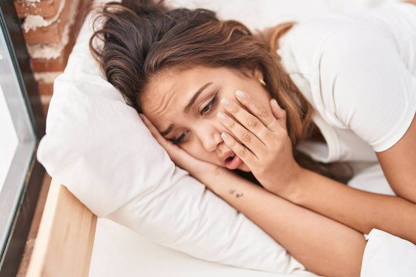 Joven hermosa mujer hispana estresada acostada en la cama en el dormitorio - Foto, imagen