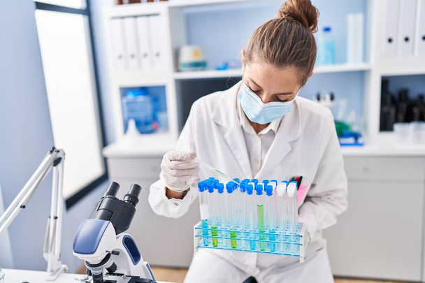 Молода жінка-науковець наливає рідину на пробірки в лабораторії
 - Фото, зображення