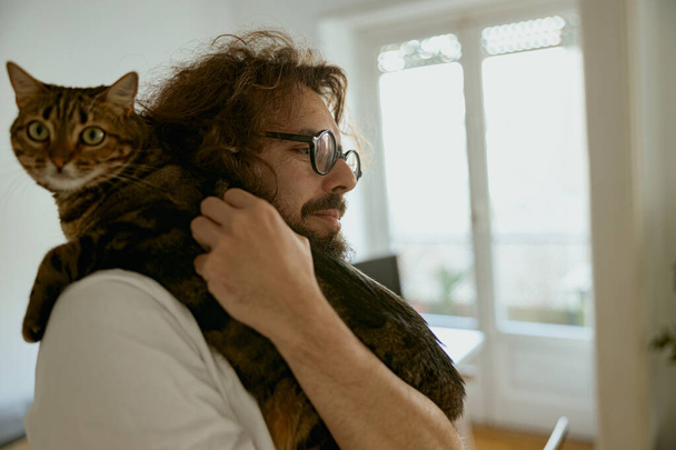Bello giovane uomo amante degli animali sta abbracciando gatto durante il tempo di riposo a casa. Foto di alta qualità - Foto, immagini