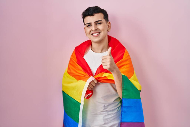 Nicht binäre Person mit Regenbogen-lgbtq-Fahne lächelt glücklich und positiv, Daumen hoch tut ausgezeichnet und Zustimmung Zeichen  - Foto, Bild
