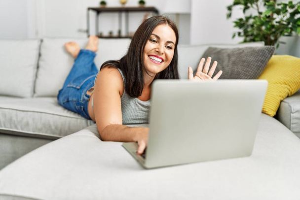 Młoda piękna latynoska kobieta mając wideo połączenie leżące na kanapie w domu - Zdjęcie, obraz