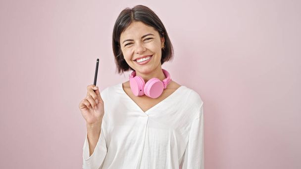 Joven mujer hispana hermosa usando auriculares con idea sobre fondo rosa aislado - Foto, Imagen