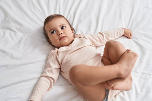 Liebenswertes hispanisches Baby im Bett liegend mit entspanntem Gesichtsausdruck im Schlafzimmer - Foto, Bild